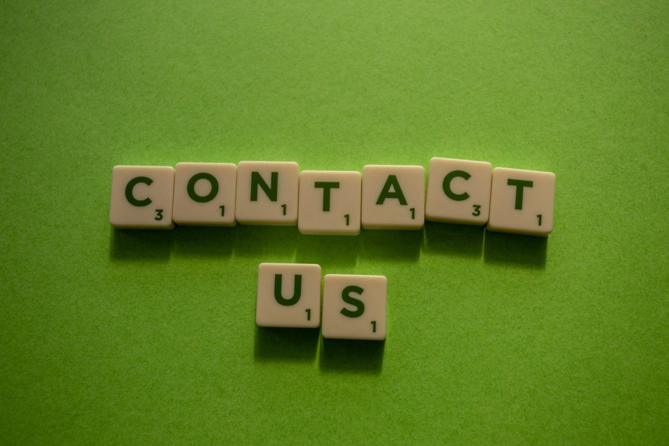 The words "Contact Us" spelled out with scrabble tiles, on a green background